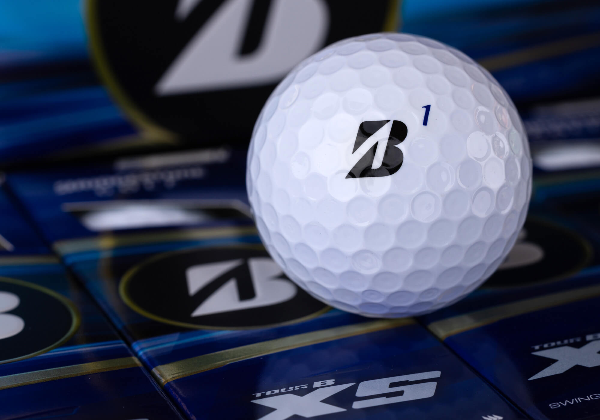 A #1 Bridgestone TOUR B XS golf ball on bright blue packaging.
