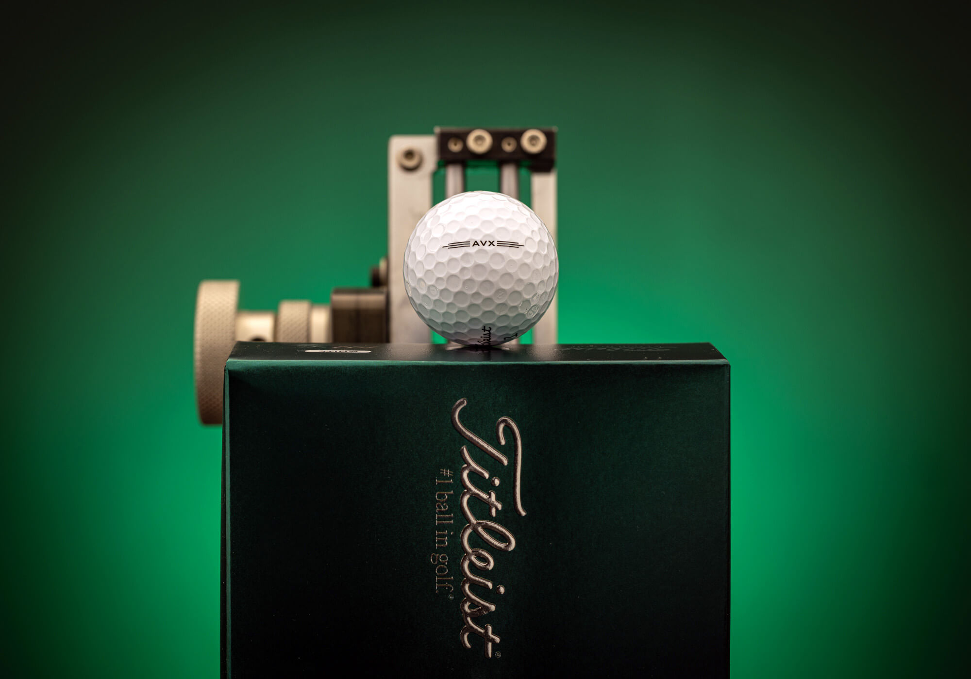 A Titleist AVX golf ball resting in a box against a backlit green background.