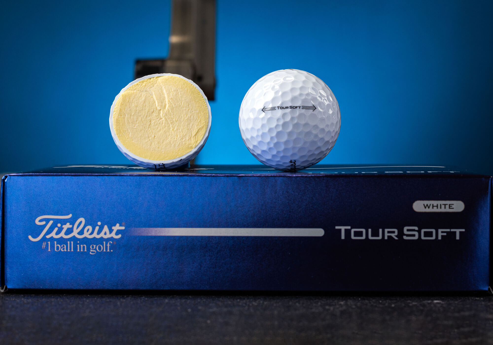 A full Titleist tournament soft golf ball that rests in a box next to the ball cut in half revealing the core.